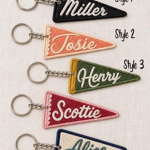 May include: Five triangular embroidered keychains with metal rings. The keychains feature the names Miller, Josie, Henry, Scottie, and Alice in various colors and styles. The text Style 1, Style 2, and Style 3 is printed next to the keychains.