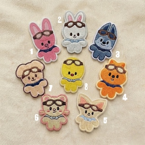 Peut inclure: Écussons brodés représentant divers animaux, dont un lapin rose, un lapin blanc, un chien bleu, un chat orange, un renard beige, un ours beige, un poussin jaune et un chien beige. Chaque écusson porte des lunettes d'aviateur et une écharpe.