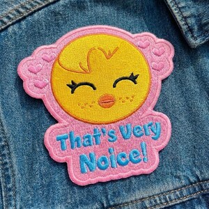 Pu&ograve; includere: Toppa ricamata con un pulcino giallo con occhi chiusi e un piccolo becco arancione, circondato da un bordo rosa con cuori. La toppa presenta la scritta "That's Very Noice!" in blu.