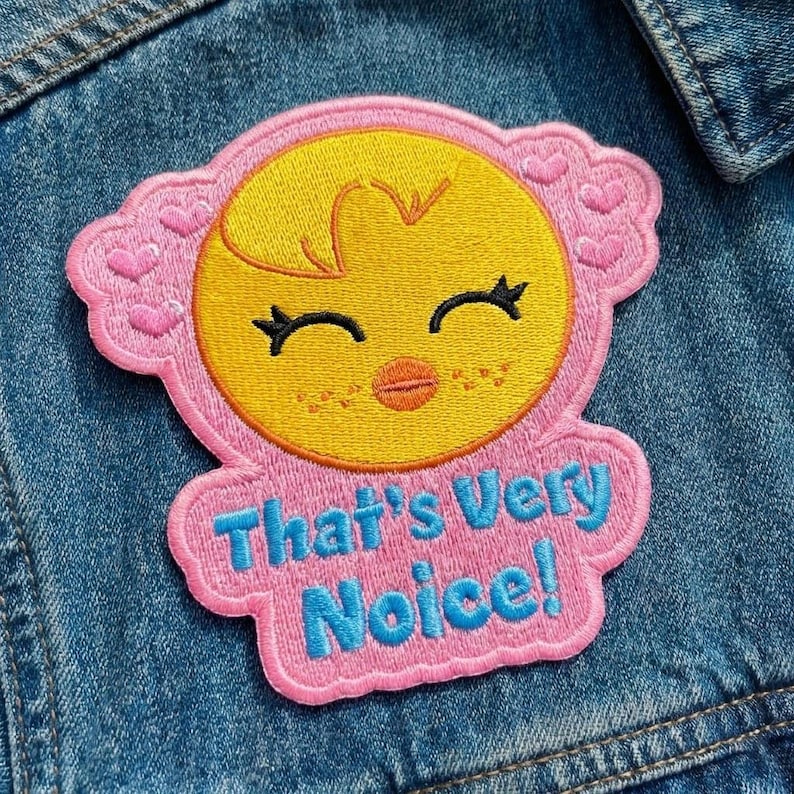 Pu&ograve; includere: Toppa ricamata con un pulcino giallo con occhi chiusi e un piccolo becco arancione, circondato da un bordo rosa con cuori. La toppa presenta la scritta "That's Very Noice!" in blu.