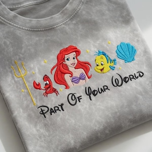 Puede incluir: Camiseta gris con un dise&ntilde;o bordado de Ariel, Flounder, Sebasti&aacute;n y una concha azul. La frase "Part Of Your World" est&aacute; bordada debajo de los personajes. Un tridente dorado y estrellas amarillas completan el dise&ntilde;o.
