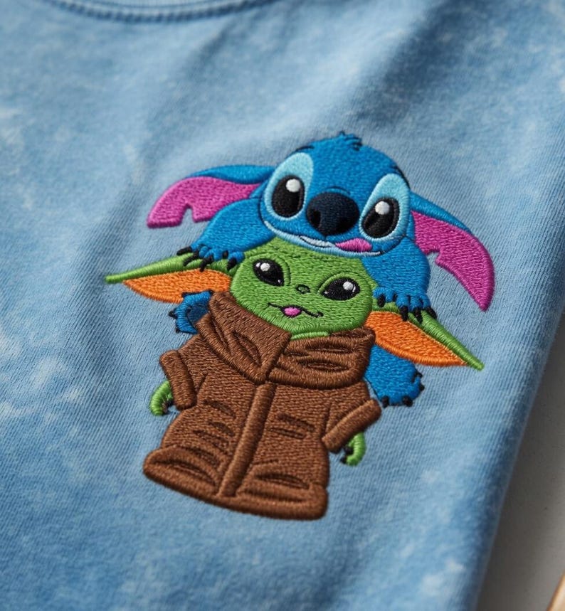 May include: Embroidered design of Stitch and Grogu (Baby Yoda) on light blue fabric. Stitch is blue with pink ears, Grogu is green with a brown coat. The design is centered on the fabric.