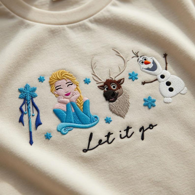 Puede incluir: Sudadera bordada de color crema con Elsa, Olaf y Sven de Frozen. El dise&ntilde;o incluye copos de nieve azules y la frase "Let it go" en escritura negra. Los personajes est&aacute;n representados en colores vibrantes.