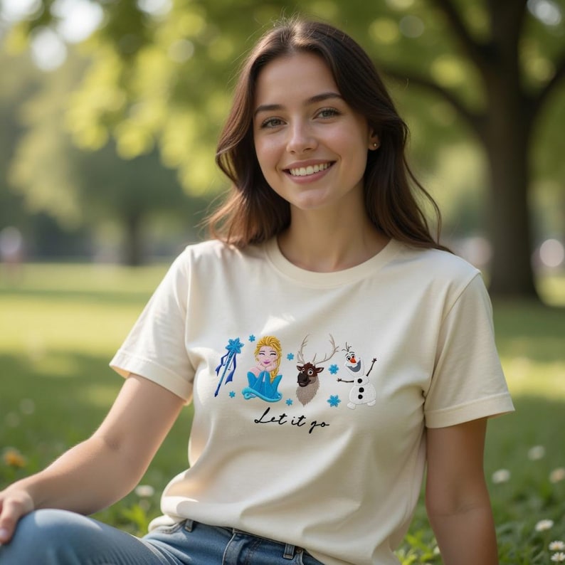 Puede incluir: Camiseta color crema con un gr&aacute;fico de una princesa, un reno y un mu&ntilde;eco de nieve, con el texto "Let it go". El dise&ntilde;o incluye detalles en azul y blanco. La camiseta est&aacute; hecha de un material suave.