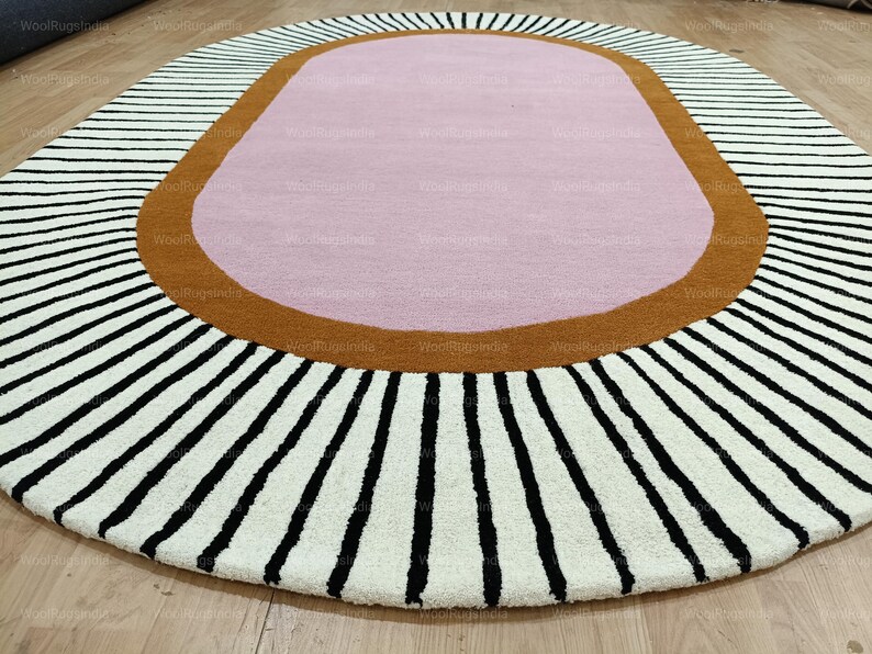 Pu&ograve; includere: Un tappeto ovale con un centro rosa, circondato da un bordo marrone e un campo bianco con strisce nere che si irradiano verso l'esterno. Il tappeto &egrave; progettato per essere posizionato su un pavimento in legno.