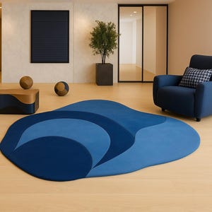 May include: A modern living room featuring a blue area rug with an abstract design. A navy blue armchair with a patterned pillow sits nearby. A dark blue and gold coffee table and decorative spheres complete the scene. The room has light wood flooring.