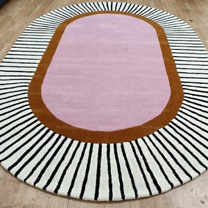 Pu&ograve; includere: Tappeto ovale con centro rosa, bordo marrone e bordo esterno a righe bianche e nere. Il design del tappeto &egrave; moderno e adatto a un soggiorno o una camera da letto. Lunghezza: circa 180 cm.