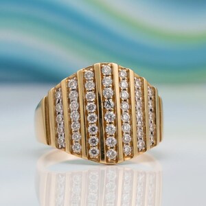 May include: A gold ring with a rectangular face, adorned with vertical rows of small, sparkling diamonds. The ring's band is a solid gold color, and the diamonds are set closely together, creating a brilliant display. The ring is displayed on a reflective surface.