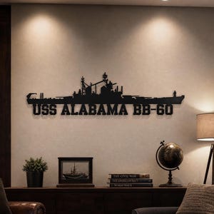 Può includere: Un'opera d'arte da parete in metallo nero che raffigura la sagoma della corazzata USS Alabama BB-60, con dettagli su alberi, torrette e strutture dello scafo, con il testo USS ALABAMA BB-60 in grassetto maiuscolo sotto la nave.
