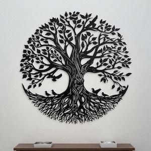 May include: Black metal tree of life wall art. The circular design features a detailed tree with leaves, branches, and roots, with birds perched on the branches and roots. The artwork is mounted on a white wall, creating a striking contrast.
