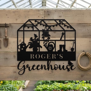 May include: Black metal greenhouse sign with the text "Roger's Greenhouse". The sign features silhouettes of gardening tools, plants, and a bird. It is mounted on a wooden wall with a rope coil.