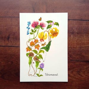 May include: A white rectangular print featuring a watercolor illustration of Vermont state flora including red clover, yellow lilies, maple leaves, and pitcher plants. A small butterfly and bee are present. The word Vermont is written in black script.