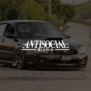 Puede incluir: Coche negro con la palabra "ANTISOCIAL" en blanco, con caracteres japoneses debajo. El coche tiene una toma de aire en el capó y una pancarta "Hundreds" en el parabrisas. La matrícula dice "6UDR811".