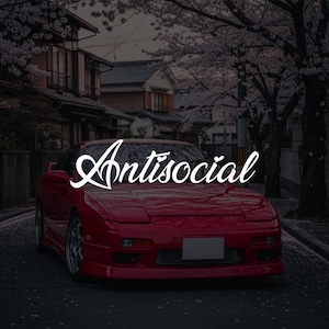 May include: A red sports car with the word "Antisocial" in white script is parked on a street. The background shows Japanese buildings and cherry blossom trees in bloom.