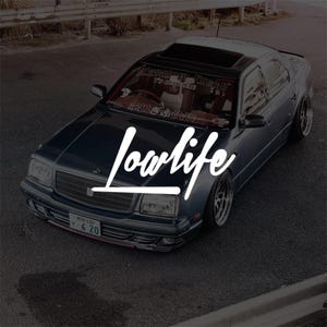 May include: Dark teal sedan with the word "Lowlife" in white script across the front. The car has a sunroof, custom wheels, and a license plate. The car is parked on asphalt.