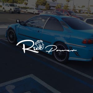 Peut inclure: Une voiture coupé turquoise avec des jantes noires est garée dans un parking. La voiture porte un logo blanc qui dit "Rice Power" dans une police stylisée. D'autres voitures sont visibles en arrière-plan.