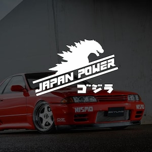 Peut inclure: Une voiture de sport rouge avec le texte "JAPAN POWER" et des caractères japonais, ainsi qu'une silhouette blanche de Godzilla. La voiture a des détails noirs et les logos "NISMO" et "SKYLINE".