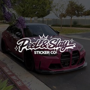May include: A dark magenta saloon parked on the side of the road with a white graphic logo overlaid in the centre that reads Peel & Slay STICKER CO, featuring a crown icon above the text and small star accents on the left and right sides.