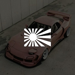 May include: A rose-colored sports car with a white rising sun emblem. The car has a spoiler, white wheels, and a low profile. The image is taken from a high angle, showing the car on a concrete surface.