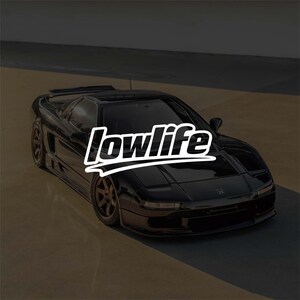 May include: A black Honda NSX sports car featuring a low-profile design, a rear spoiler, and dark-coloured wheels. The word "lowlife" is written in large, bold, white stylised letters across the centre of the vehicle's bonnet and windscreen area.