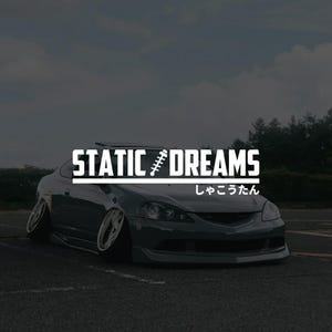 May include: A grey sports car with a lowered suspension is parked on asphalt. The car has silver rims and a front spoiler. The text "STATIC DREAMS" is displayed in white above the car, with Japanese text below.