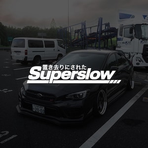 May include: A black saloon car parked in a lot with the white text "置き去りにされた Superslow" overlaid on the centre. The vehicle features a front grille emblem, a front number plate reading "とちぎ 309 20-00", and low-profile tyres on metallic rims.