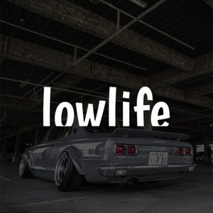 Peut inclure: Une voiture grise vintage avec le mot "lowlife" en texte blanc. La voiture est garée dans un garage, mettant en valeur sa suspension abaissée et ses roues personnalisées. La voiture a un aileron arrière et une plaque d'immatriculation japonaise.