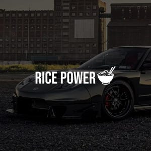 May include: A black sports car with the text "RICE POWER" in white, and a white bowl of noodles graphic. The car is parked on gravel, with industrial buildings in the background.