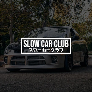 Könnte beinhalten: Ein silbernes Auto mit dem Text "SLOW CAR CLUB" in einem weißen Rechteck. Japanischer Text steht darunter. Das Auto steht auf einer Straße mit Bäumen im Hintergrund.
