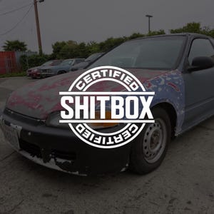 May include: A weathered saloon car with a black front bumper, a red and grey bonnet, and a blue front wing. A circular white graphic is overlaid on the centre of the bonnet, featuring the text CERTIFIED SHITBOX CERTIFIED in bold white capital letters.