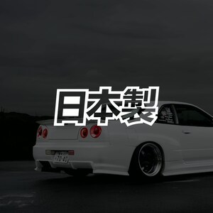 May include: A white sports car with black rims and a license plate. The Japanese text "Made in Japan" is overlaid on the image. The car has red taillights and is set against a dark gray background.