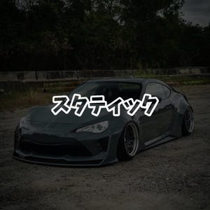 May include: Dark green sports car with the Japanese text "スタティック" across the windshield. The car is lowered and has custom wheels. The background is a blurred view of trees and a concrete barrier.