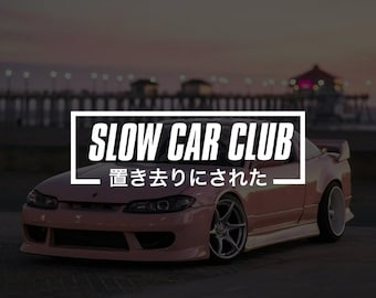 May include: A light pink sports car with a large rear spoiler and silver wheels. A white rectangular frame overlays the car, containing the text SLOW CAR CLUB in bold capital letters and the Japanese text 置き去りにされた below it.