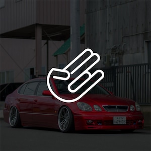 May include: A red sedan with custom wheels and a white hand gesture logo. The car is parked on a street with buildings in the background. The license plate reads "69-03".