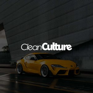 Może przedstawiać: Jasnożółty samochód sportowy o eleganckim designie zaparkowany na mokrej nawierzchni asfaltowej. Samochód ma czarne akcenty i srebrne felgi. Tekst "Clean Culture" jest wyświetlany na białym tle nad samochodem.
