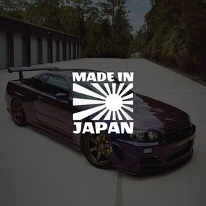 Peut inclure: Une voiture de sport violet foncé avec un aileron arrière et des roues de couleur bronze. La voiture porte un graphisme "MADE IN JAPAN" avec un soleil levant.