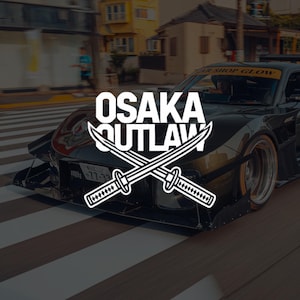 May include: A black sports car with the white text "OSAKA OUTLAW" and two crossed swords. The car is on a zebra crossing, with a blurred background of buildings and a person.
