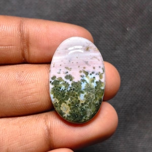 May include: An oval-shaped cabochon gemstone featuring a smooth, polished surface. The stone displays a distinct color gradient, transitioning from a soft, pale pink at the top to a deep, mossy green at the bottom with intricate floral-like patterns.