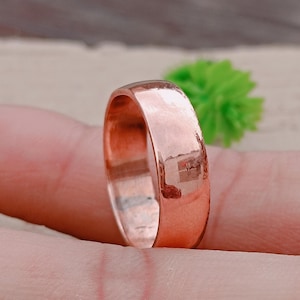 May include: A polished copper ring with a smooth, rounded band. The ring reflects light, showcasing its metallic lustre. The ring is a simple, classic design, suitable for everyday wear. The ring is a piece of jewellery.