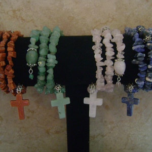Può includere: Quattro braccialetti con pietre di diversi colori e ciondoli a forma di croce argentati. I braccialetti sono realizzati con pietre rosse, verdi, rosa e blu.