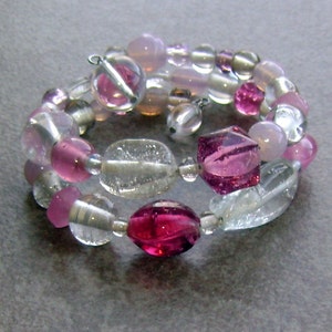 Könnte beinhalten: Ein mehrreihiges Armband mit rosa, klaren und silbernen Perlen. Das Armband besteht aus Glas- und Metallperlen.