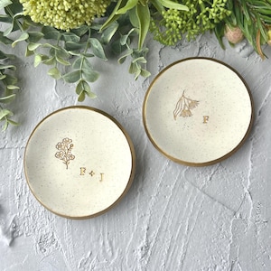 May include: Two white ceramic ring dishes with gold rims. One dish features a small floral design and the initials "F + J". The other dish has a larger floral design and the initial "F".