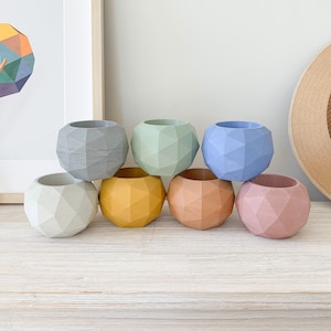 Può includere: Sei vasi geometrici in vari colori pastello, tra cui grigio, verde, blu, giallo, arancione e rosa. I vasi sono realizzati in un materiale strutturato e hanno un design unico e sfaccettato.