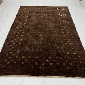 Pode incluir: Um tapete retangular marrom com um padrão detalhado. O tapete tem um fundo marrom escuro com formas e desenhos geométricos marrons mais claros. O texto "Abiba Arts" é visível no canto superior direito.