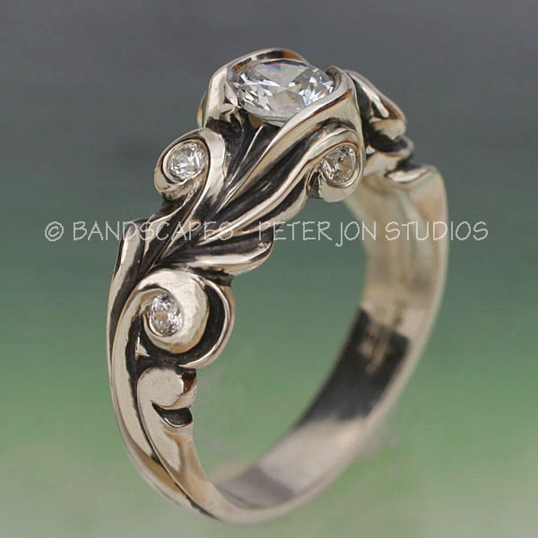 May include: A silver ring featuring a large, clear, round gemstone surrounded by smaller, clear gemstones. The band is intricately designed with swirling patterns.