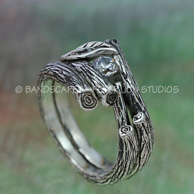 May include: A silver ring with a twig design and a clear gemstone. The ring is made to look like a bundle of twigs.