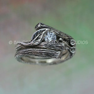 May include: A silver ring set with a single round diamond, set in a design of intertwined branches and a leaf.