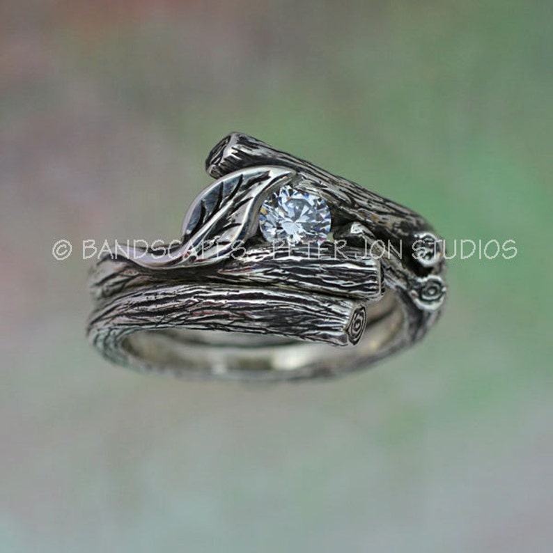 May include: A silver ring set with a single round diamond, set in a design of intertwined branches and a leaf.