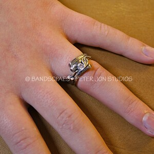 May include: A silver ring with a clear stone set in a leaf design. The ring is worn on the finger of a person's hand.