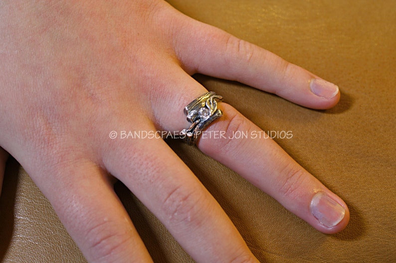 May include: A silver ring with a clear stone set in a leaf design. The ring is worn on the finger of a person's hand.